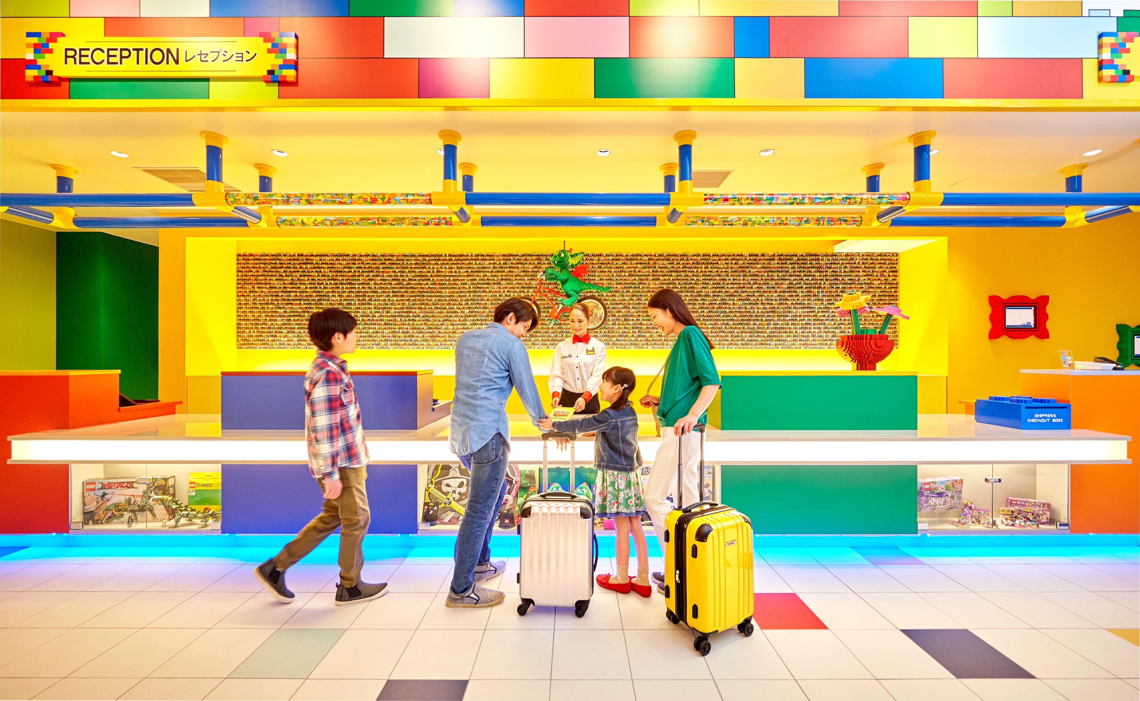 Un área de recepción luminosa y colorida con mostrador de recepción, una pared de objetos pequeños y una planta verde.