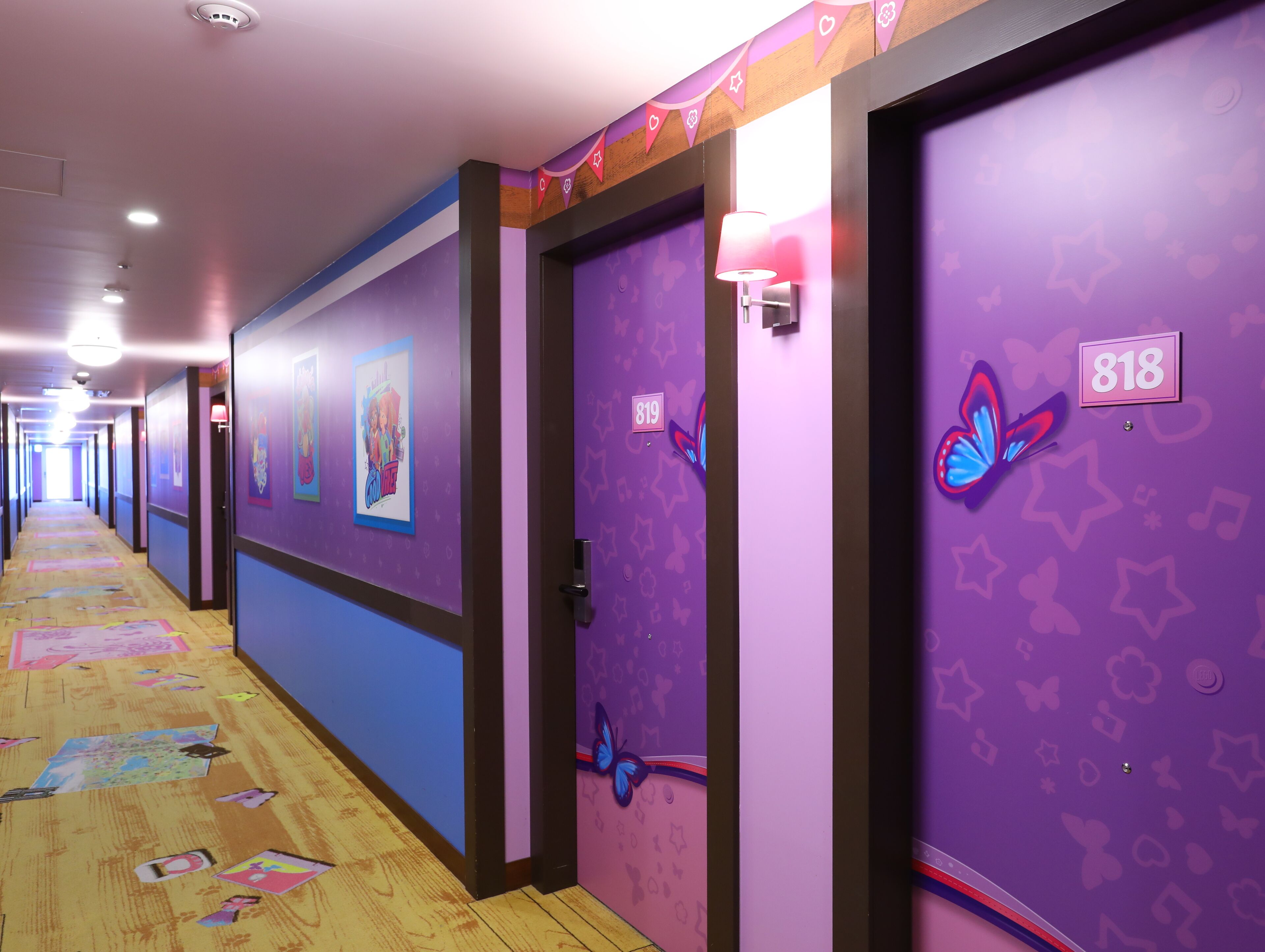 A hotel hallway with purple walls, numbered doors, and butterfly decorations.