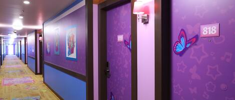 A hotel hallway with purple walls, numbered doors, and butterfly decorations.