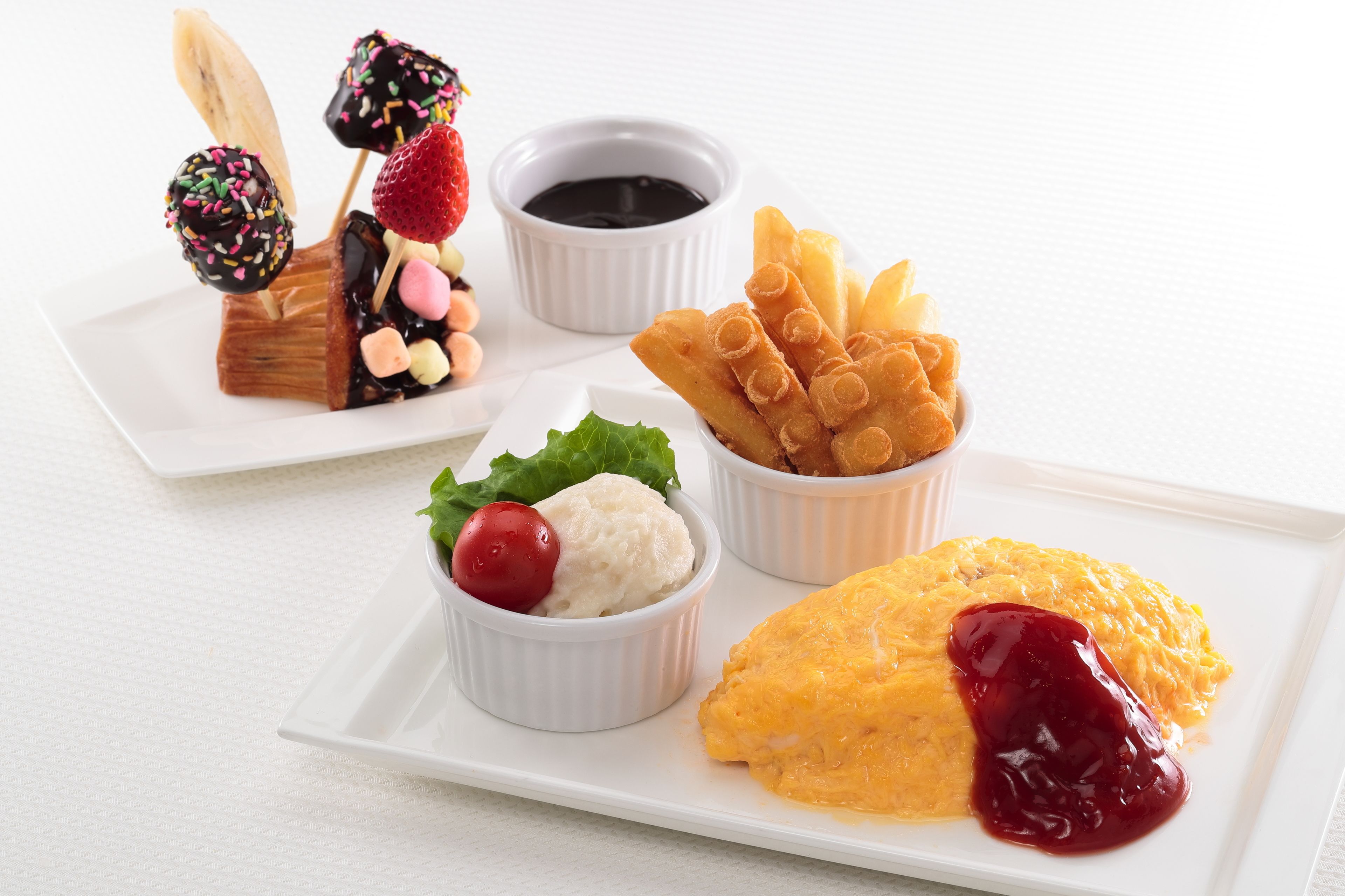 A white plate with a dessert consisting of a fruit-covered cake, a bowl of ice cream with a cherry, and a piece of cake with a berry sauce.