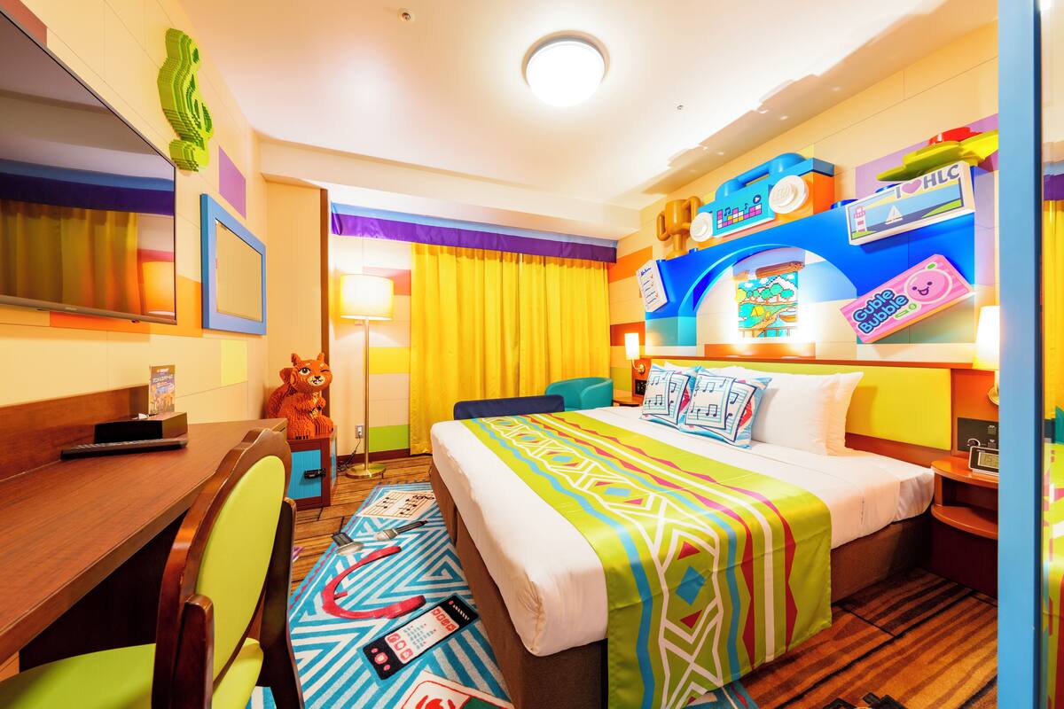 A hotel room with a bed, a desk, a chair, a TV, and a window with curtains.