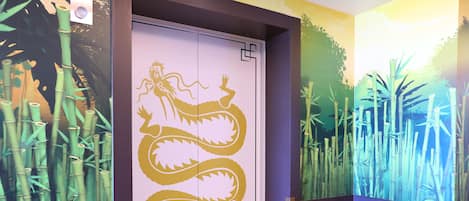 A room with a sliding door featuring a dragon design, bamboo wall art, and a colorful floor mat.