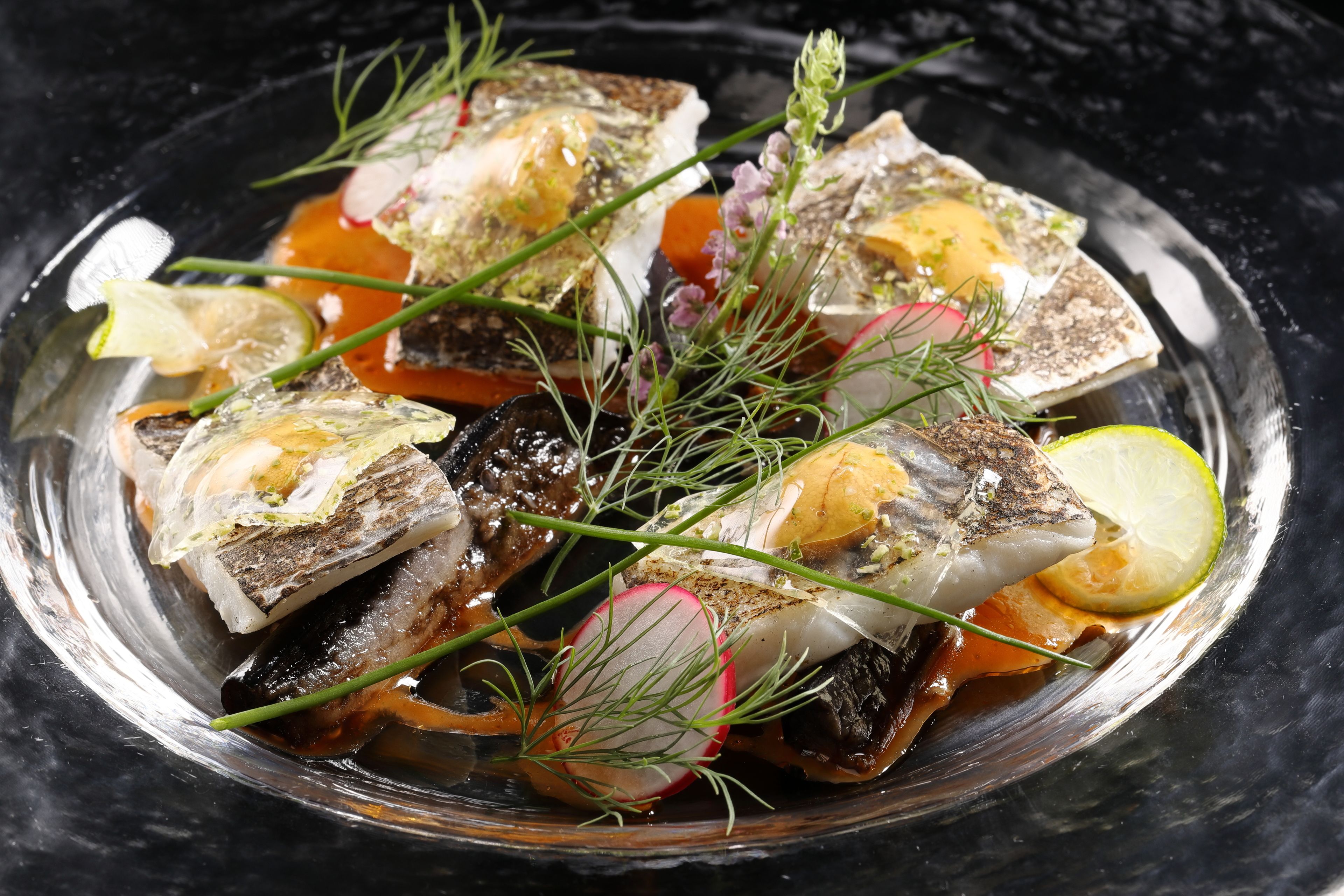 A dish of fish with herbs and lemon slices on a plate.