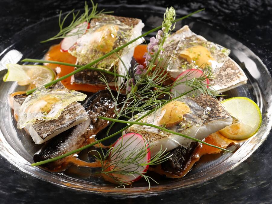 A dish of fish with herbs and lemon slices on a plate.