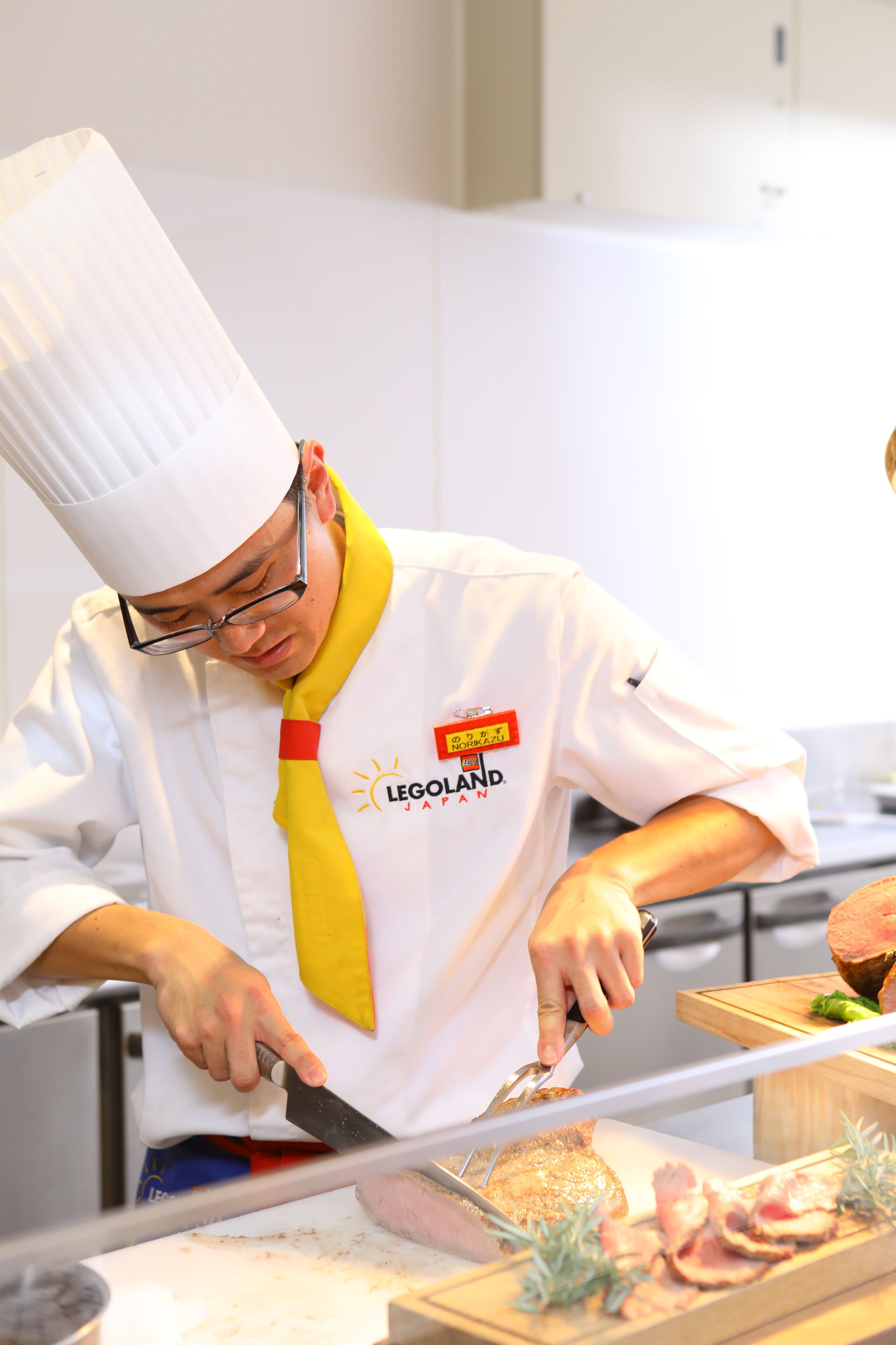 A chef in a white uniform with a yellow tie, preparing food in a kitchen.