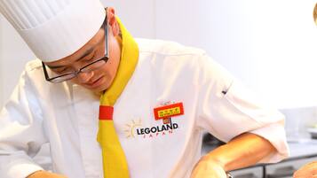 A chef in a white uniform with a yellow tie, preparing food in a kitchen.