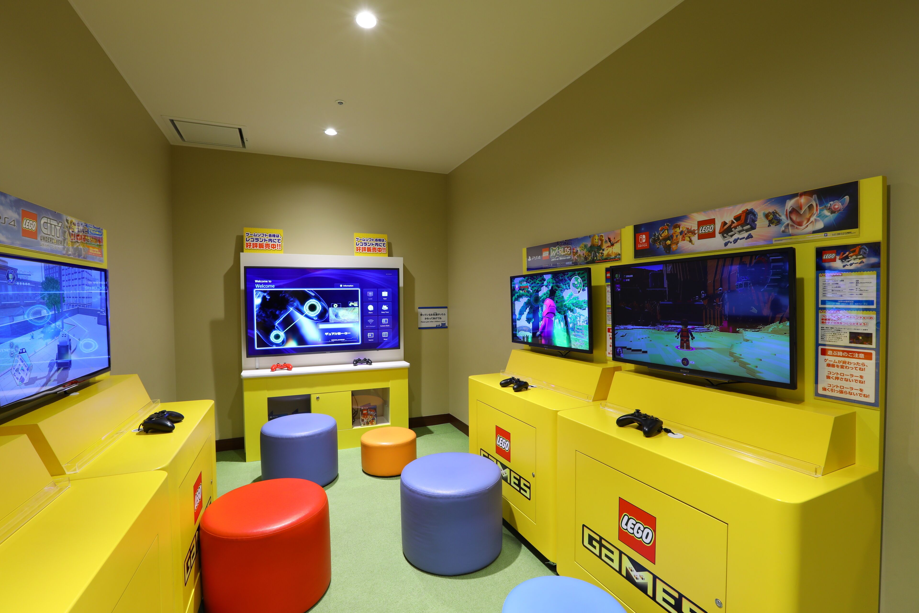 A gaming area with multiple screens, gaming consoles, and colorful stools.