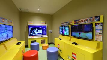 A gaming area with multiple screens, gaming consoles, and colorful stools.
