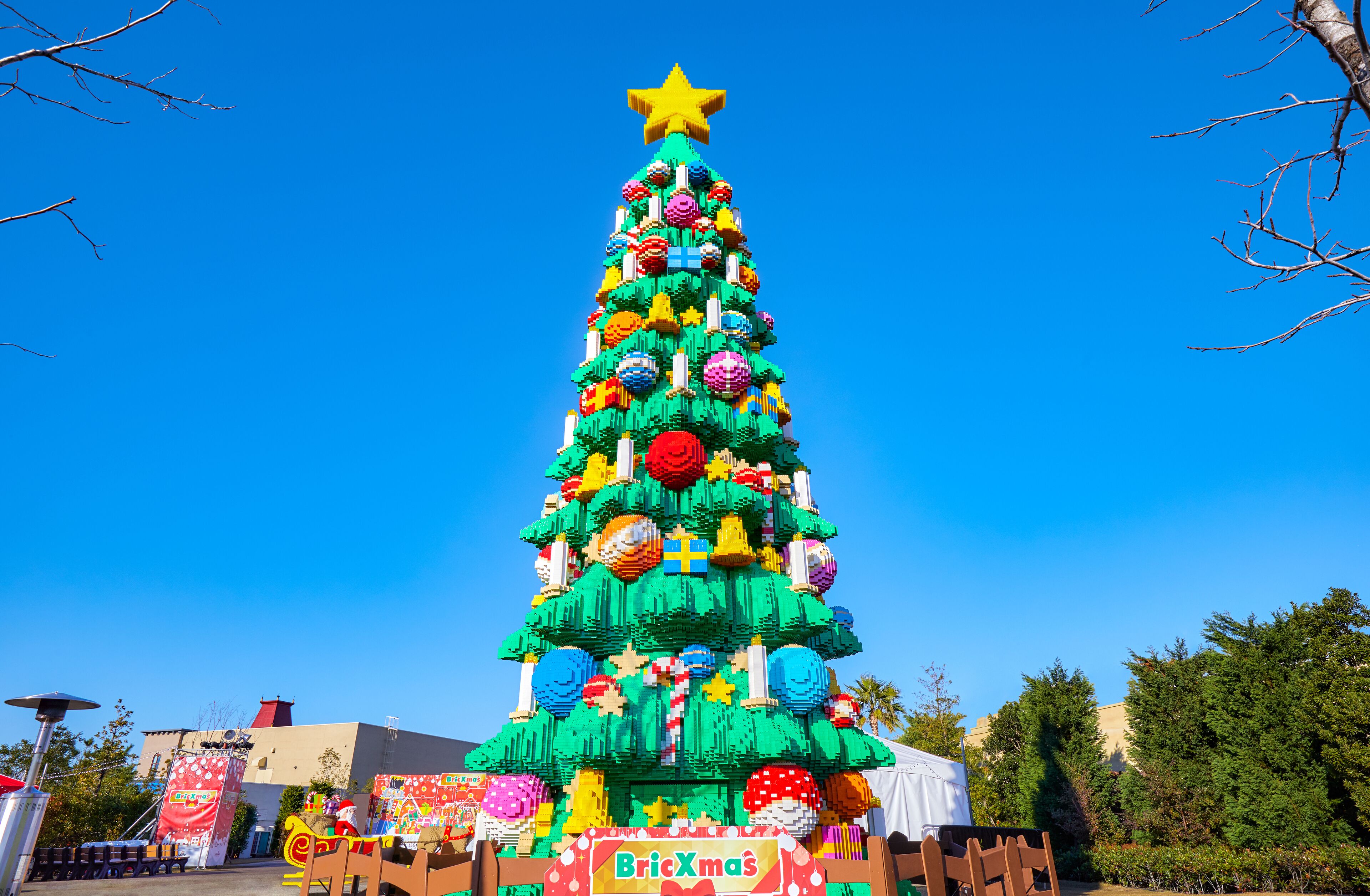 A large, colorful Christmas tree with a star on top, surrounded by various decorations and a sign that reads "BricXmas."