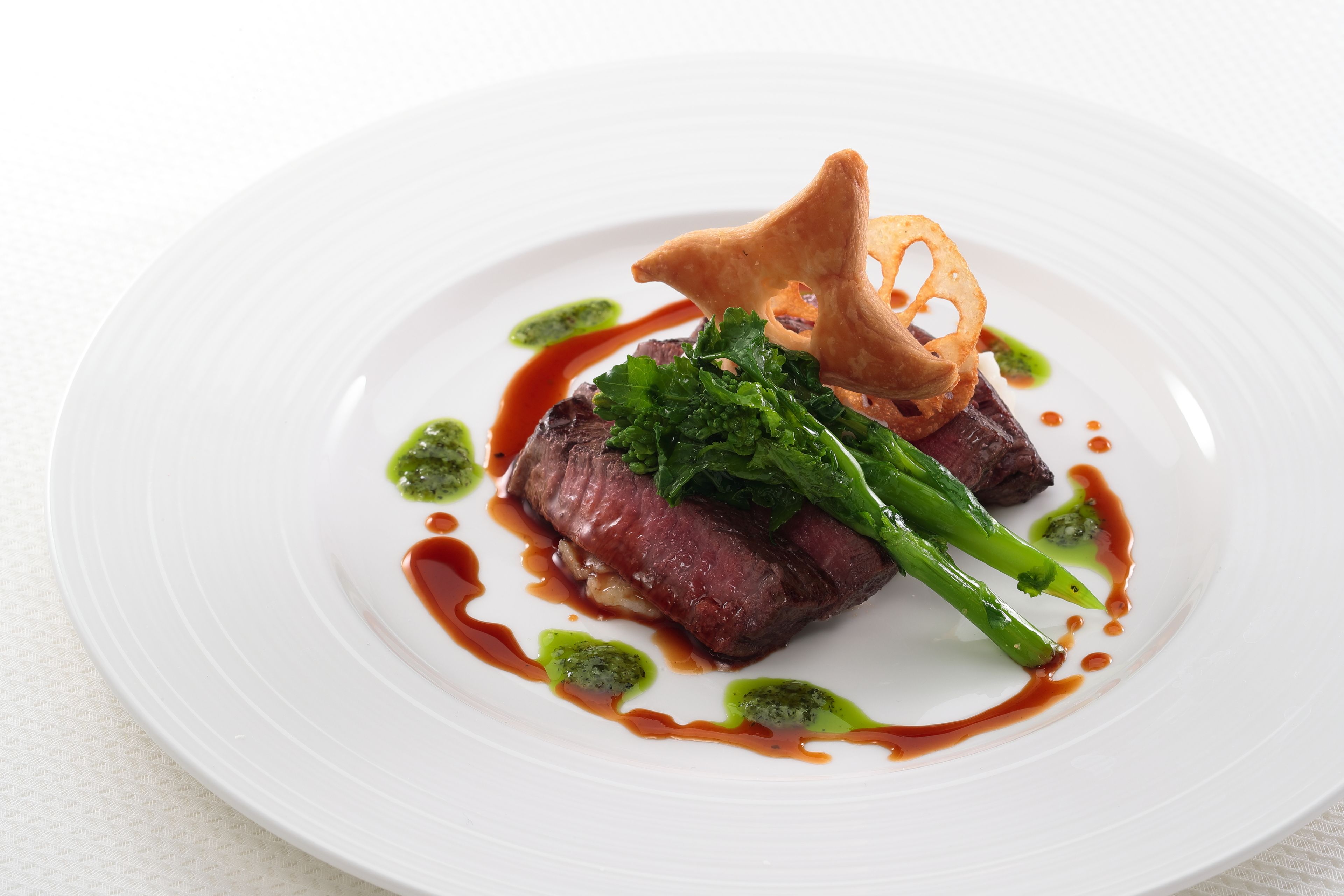 Un plato blanco con un bistec, vegetales verdes y salsa.