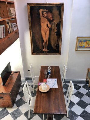 A room with a wooden table, white chairs, a laptop, a map, a candle, and a painting on the wall.