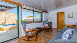 A living room with a stone wall, wooden furniture, a sofa, a wooden table, and a view of a swimming pool.