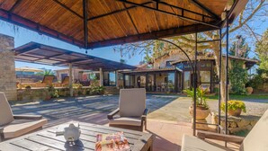 A covered outdoor patio area with wooden furniture, a table with a magazine, and potted plants.