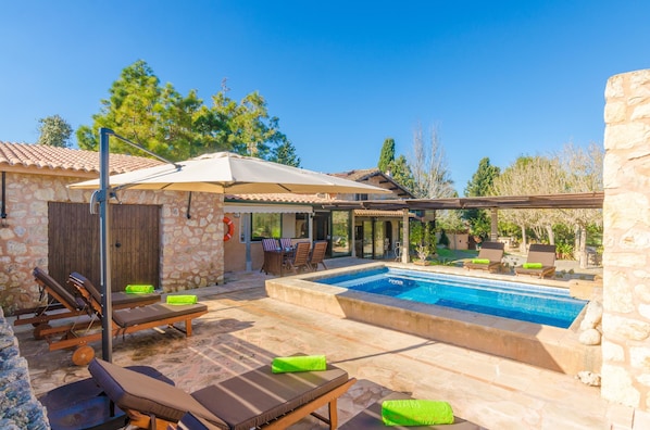 A stone building with a swimming pool, outdoor seating, and a pergola.
