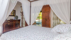 A bedroom with a canopy bed, wooden wardrobe, and a view of the outdoors.