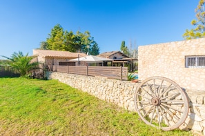 A stone wall with a rustic wooden fence, a large wheel, and a building with a tiled roof.