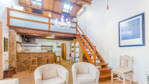 A spacious living area with a high ceiling, a wooden staircase, and a kitchen area.