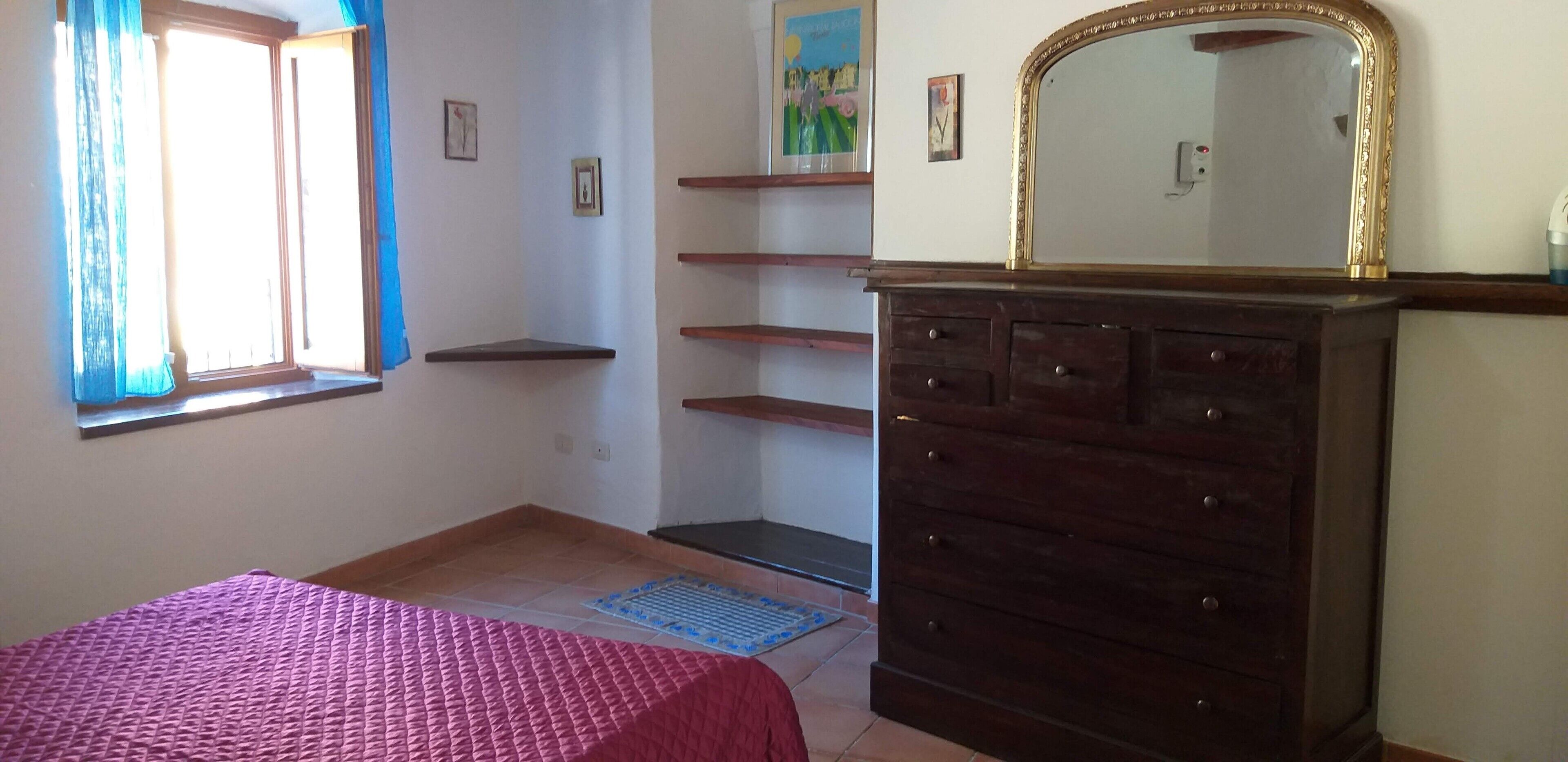 A bedroom with a bed, a dresser, a mirror, and a window with curtains.
