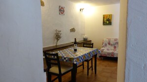 A dining area with a table covered by a checkered tablecloth, two chairs, a bottle of wine, and a vase with dried flowers.