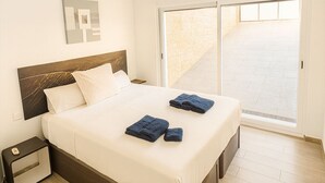 Une chambre à coucher comprenant un lit, une table de chevet, un ventilateur de plafond et une porte-fenêtre coulissante donnant sur l’extérieur.