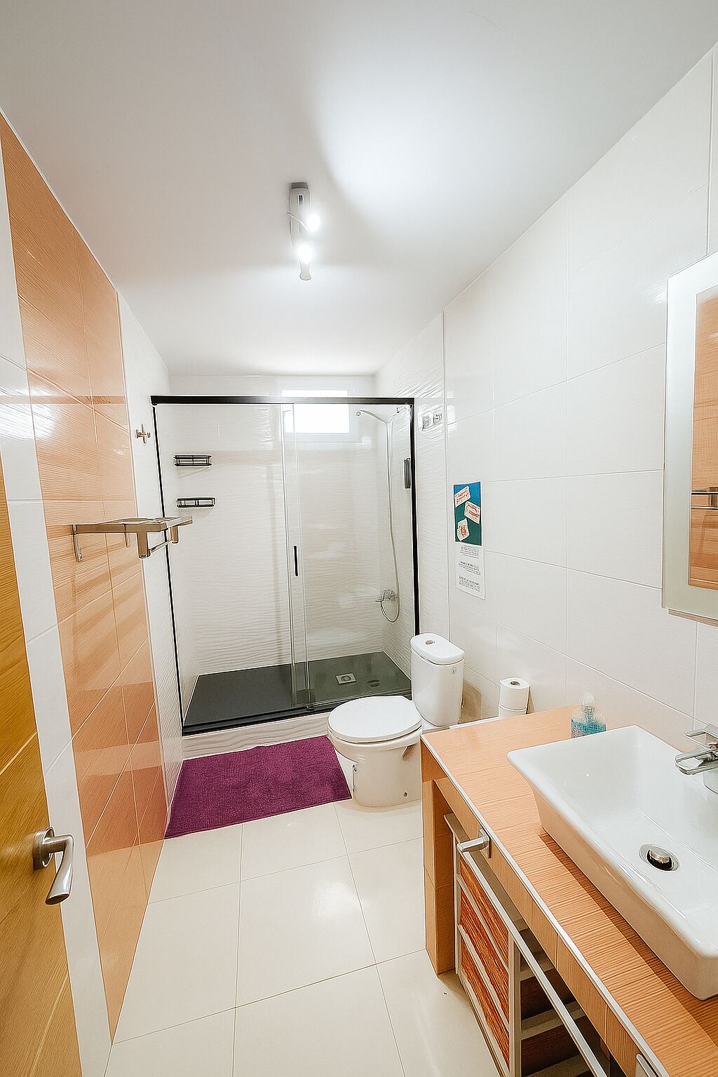 A modern bathroom with a glass-enclosed shower, a white toilet, and a wooden vanity with a sink.