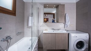 A modern bathroom with a bathtub, a sink, a mirror, and a washing machine. - Villa Arismari - "Oikos-your Cretan house" 5 mins drive from the beach (Aggeliana)