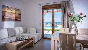 A modern living room with a sofa, a chess table, and a view of a pool and beach through a glass door. - Villa Arismari - "Oikos-your Cretan house" 5 mins drive from the beach (Aggeliana)