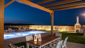 An outdoor pool area with a pergola, lounge chairs, and a table with chairs.