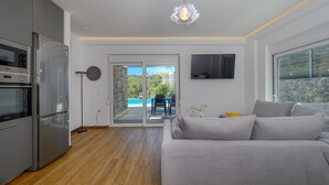 A modern kitchen with a built-in oven and microwave, a grey sofa, and a TV mounted on the wall. - Kalostous villa 2, Pool,Great location & Views (Agia Triada)