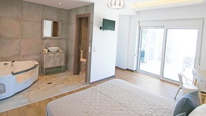 A modern bedroom with a large bed, a built-in bathtub, a vanity with a mirror, and a television. - Kalostous villa 2, Pool,Great location & Views (Agia Triada)