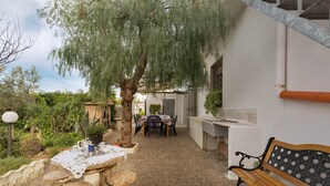 Un espace extérieur aménagé en terrasse, avec une table dressée pour les repas, un banc en bois et une pergola offrant de l’ombre.
