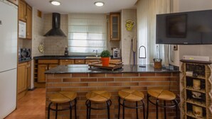 A kitchen with a central island, wooden stools, a TV, and a brick backsplash. - INNOUTHOME PERFECT APARTMENT FOR HOLIDAYS, WIFI AND AIR_CATALUNYA APARTMENT (L'Ametlla de Mar)