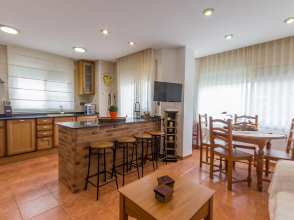 A compact kitchen with a central island, bar stools, and a dining area with wooden chairs and a table. - INNOUTHOME PERFECT APARTMENT FOR HOLIDAYS, WIFI AND AIR_CATALUNYA APARTMENT (L'Ametlla de Mar)