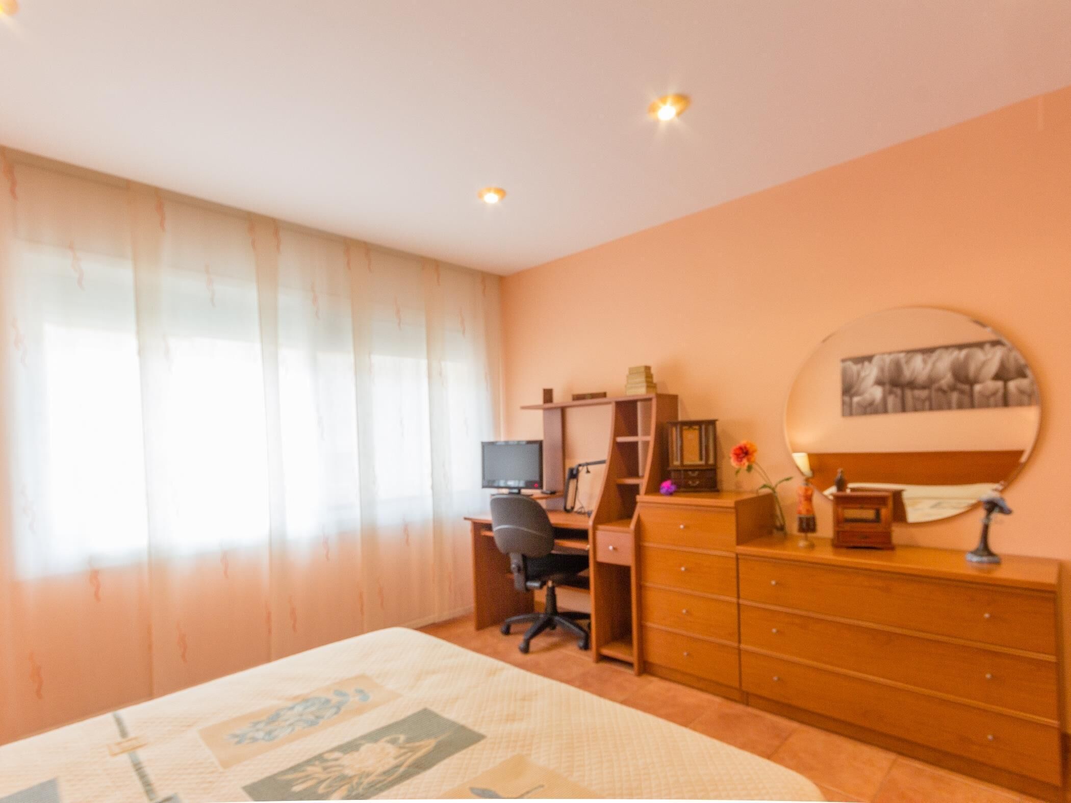Un dormitorio con cama, escritorio, silla, cómoda y ventana con cortinas.