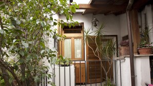 Ein kleines Haus mit Holztür, einem Fenster mit Rollläden und einem Balkon mit Blumentöpfen.