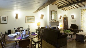 Ein gemütliches Wohnzimmer mit Holzbalkendecke, Kamin, Esstisch mit Stühlen und einer Couch.