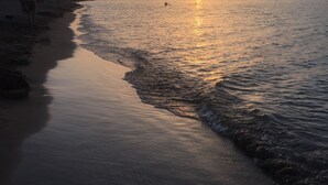 Una playa con atardecer, agua tranquila y montañas al fondo.