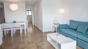 A modern living room with a teal sofa, a white coffee table, and a dining area with white chairs and a glass table.