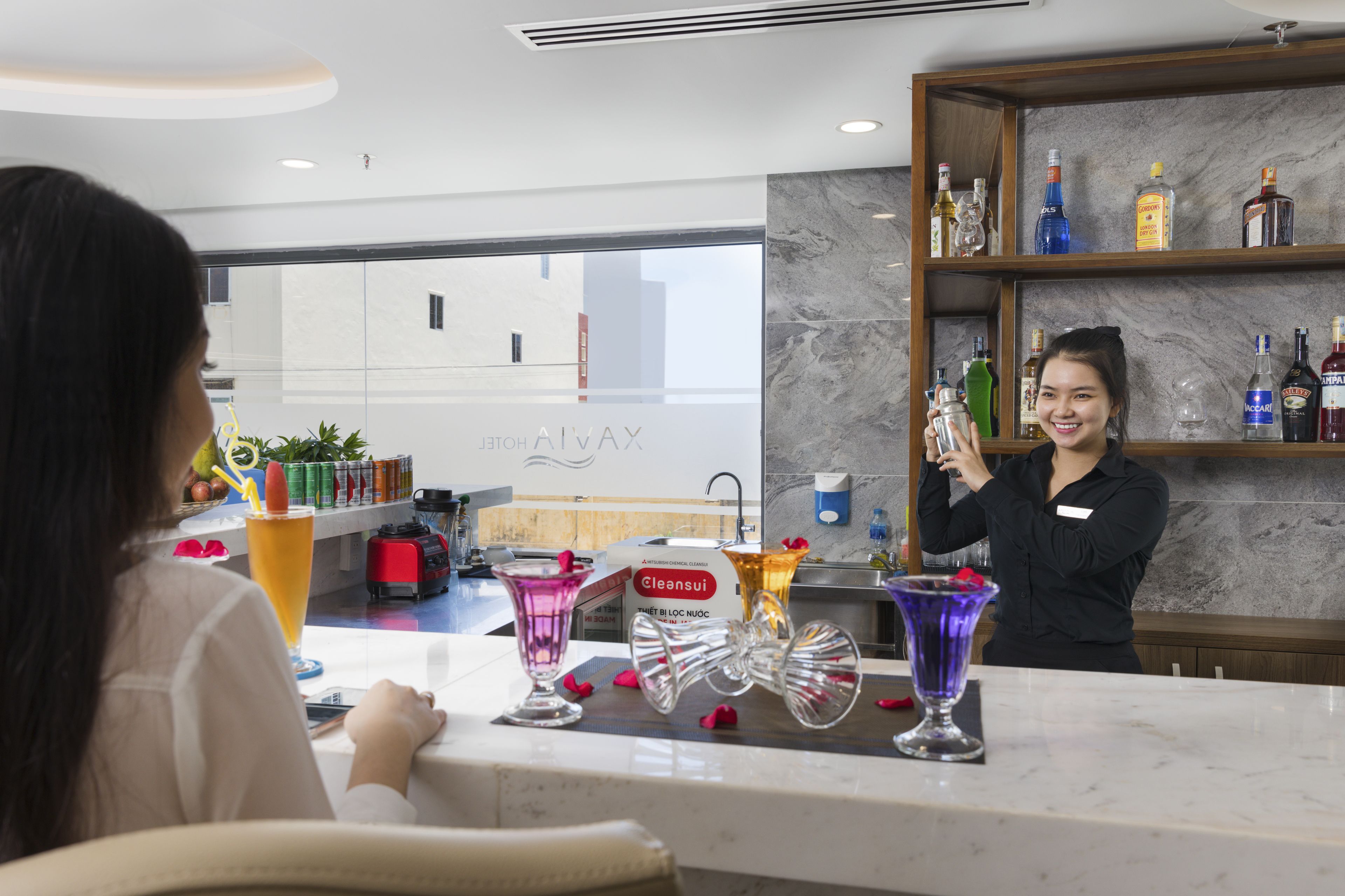 A bar area with a marble countertop, various liquor bottles, and a barista preparing a drink.