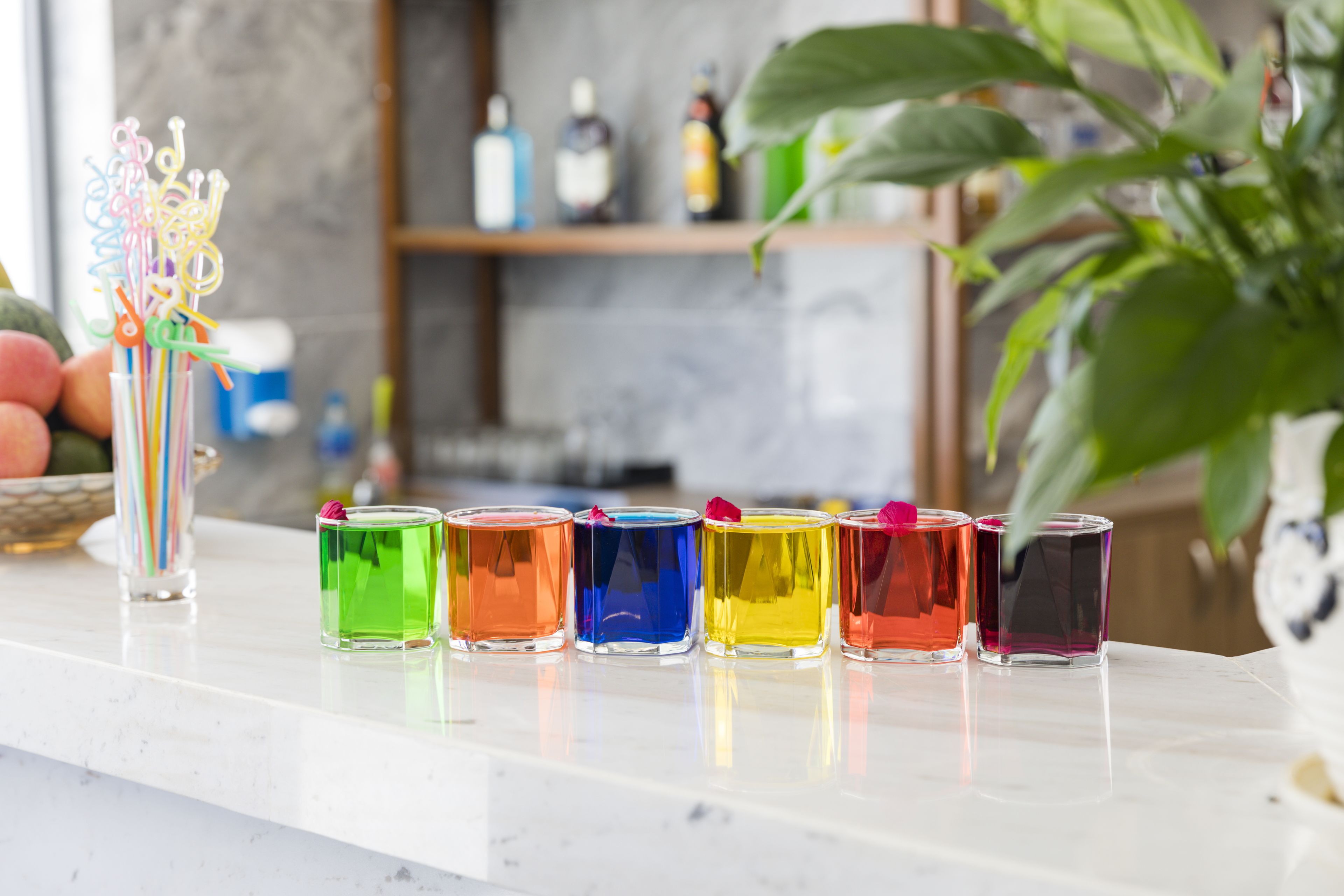 A countertop with six colorful shot glasses lined up.