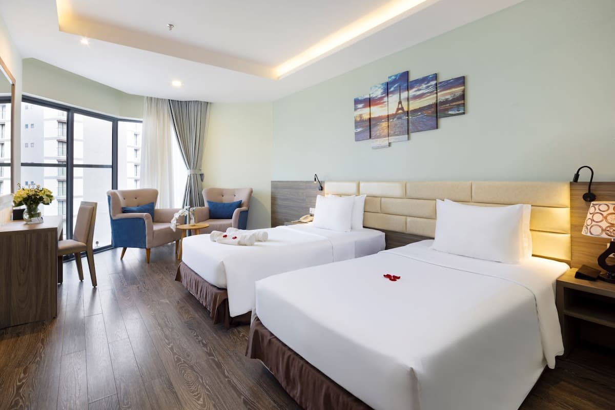 A hotel room with two beds, a desk, a chair, and a large window.