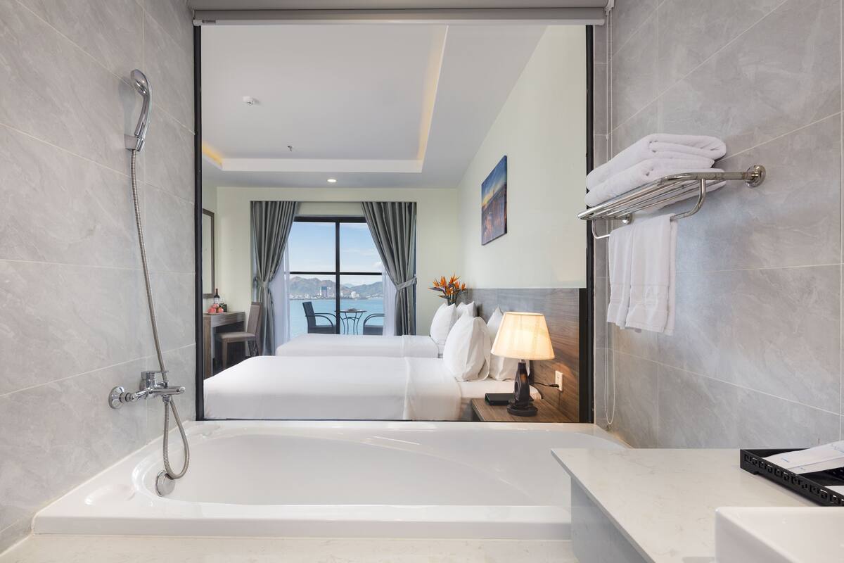 A modern hotel bathroom with a large bathtub, a shower, and a view of a balcony with a table and chairs.