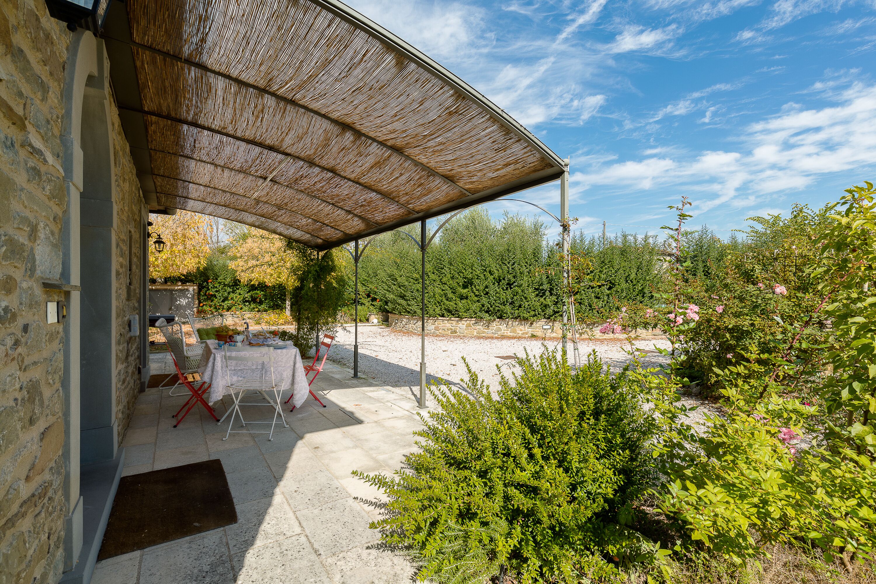 Zona exterior amb terrassa coberta, parets de pedra i vegetació als voltants.