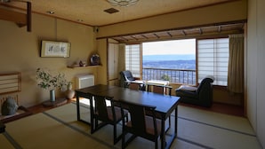 A traditional Japanese-style room with tatami flooring, a low table with chairs, a view of the city through shoji screens, and a ceiling fan. - Shiroyama inn (Ikoma)