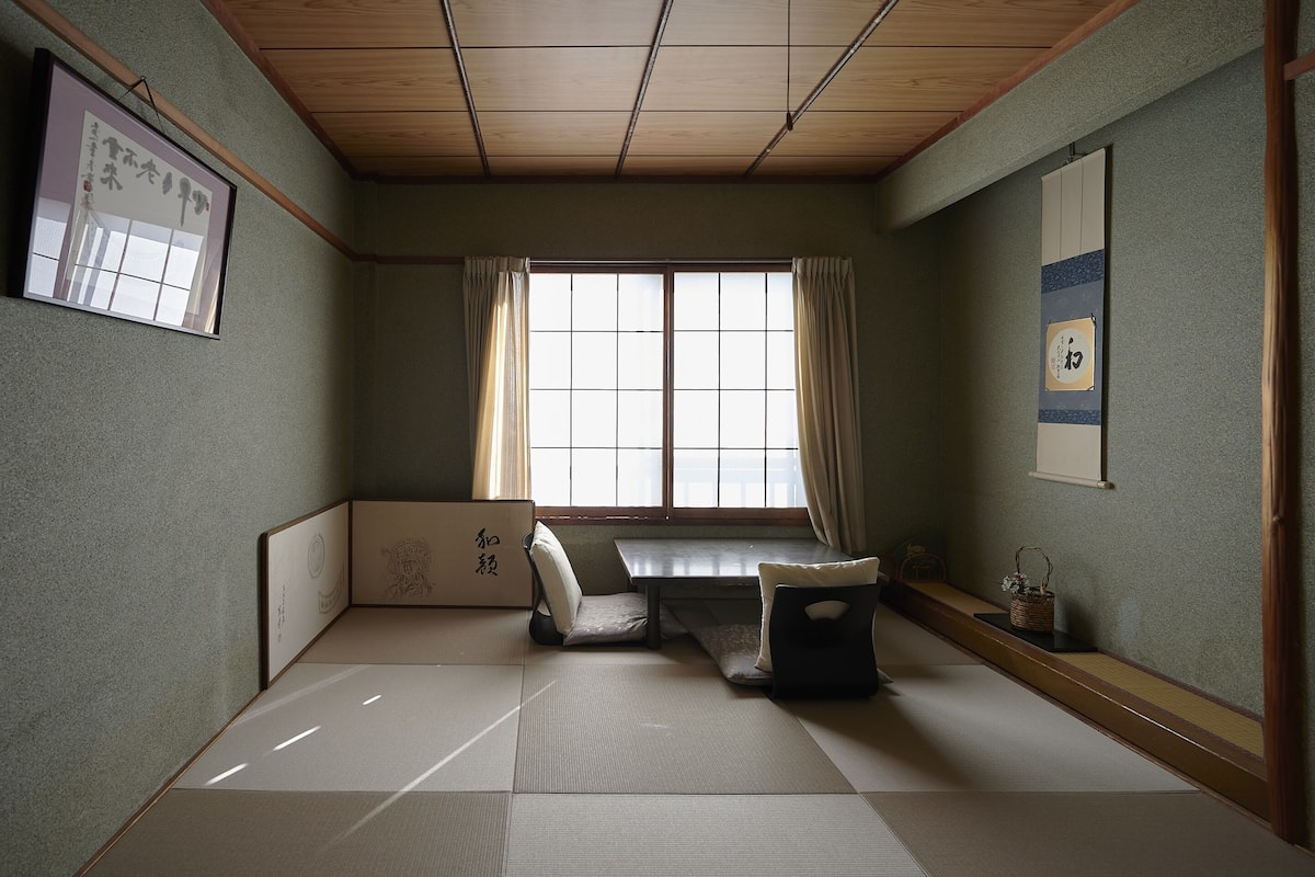 A traditional Japanese room with tatami flooring, a low table, a cushion, and a sliding door.
