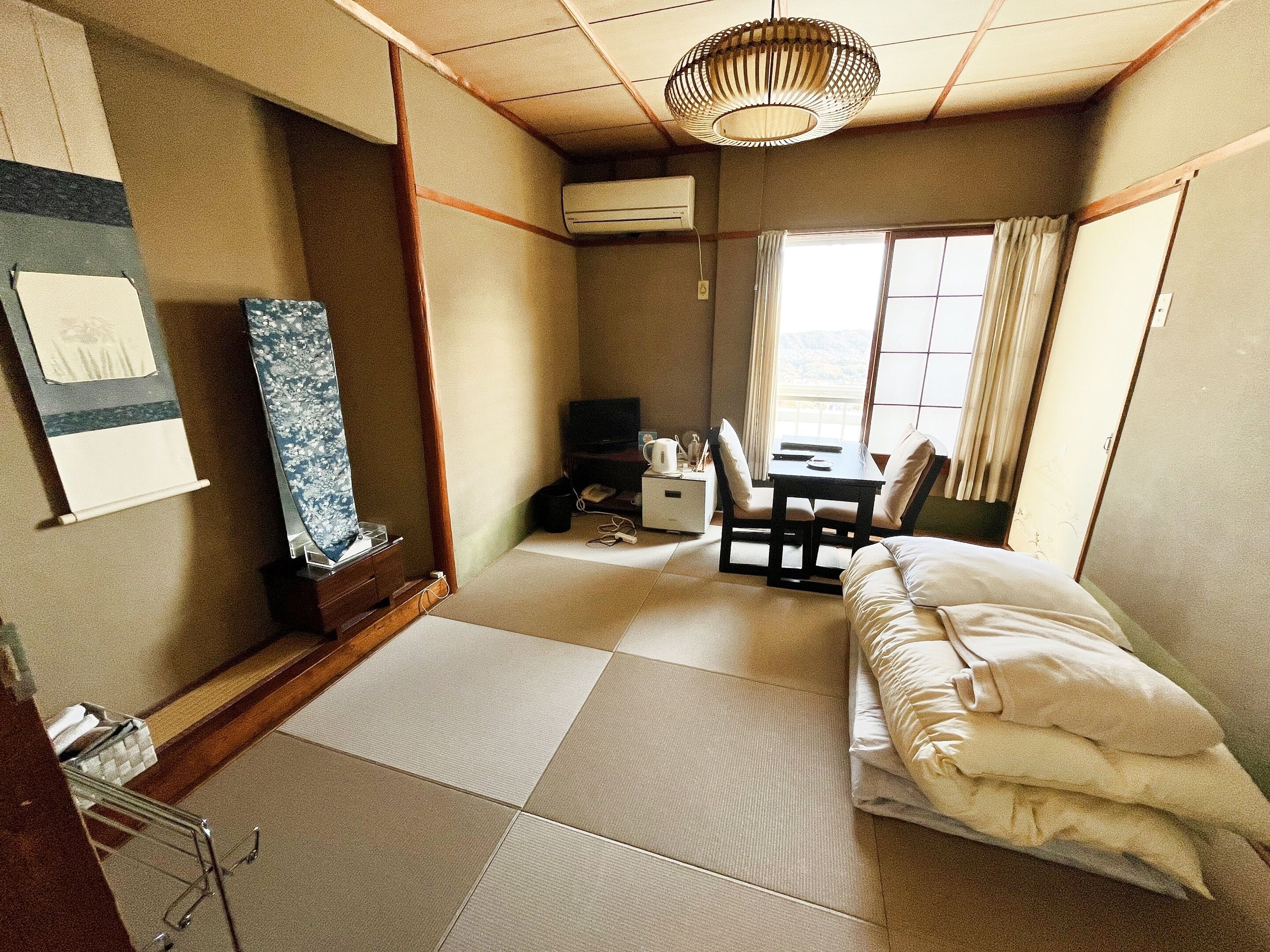 A traditional Japanese-style room with tatami flooring, a futon bed, a small desk with a chair, and a television.