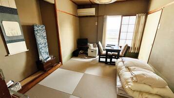 A traditional Japanese-style room with tatami flooring, a futon bed, a small desk with a chair, and a television.