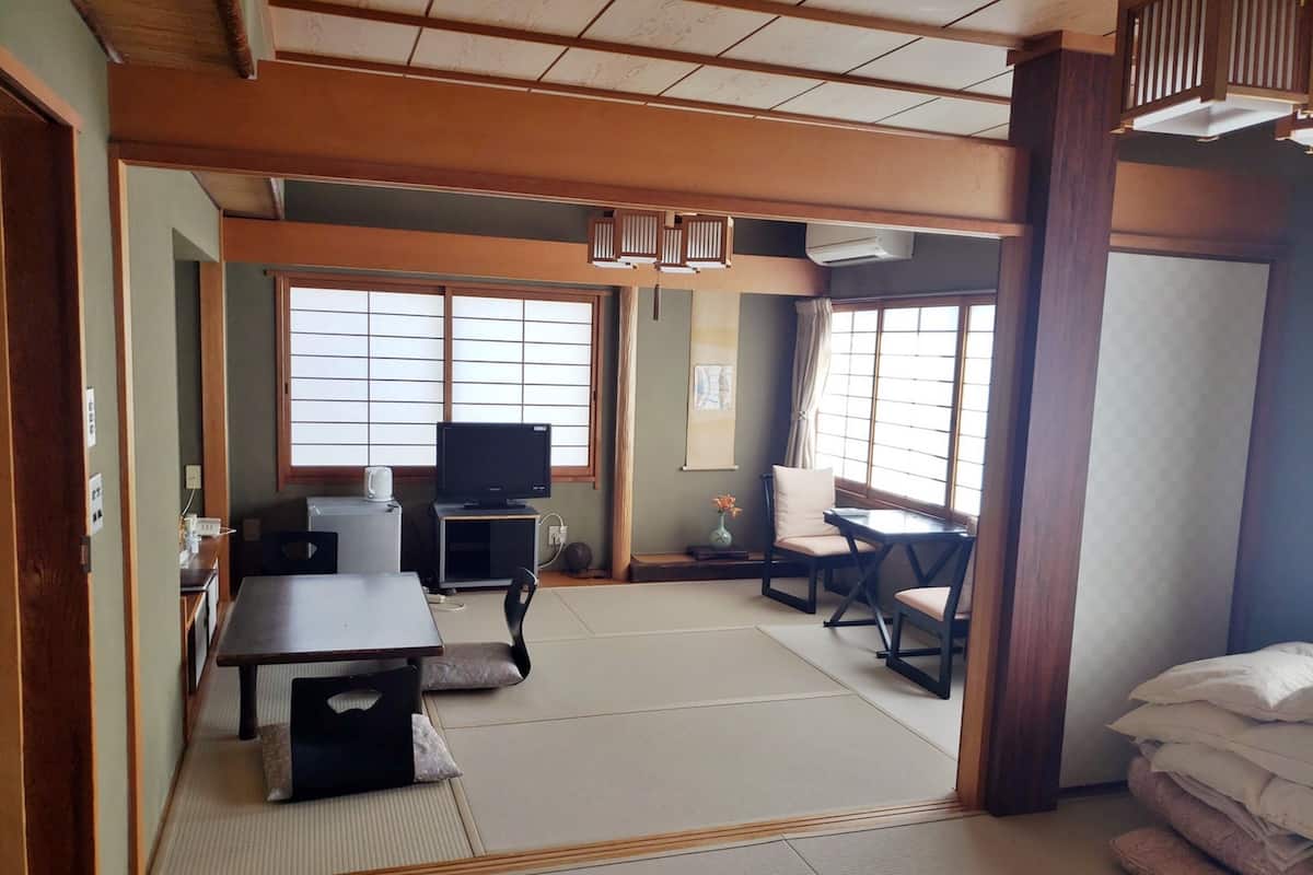 A traditional Japanese room with tatami flooring, a tatami mat table, a television, and a futon bed.