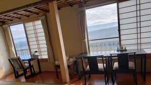 A traditional Japanese room with tatami flooring, a low table with chairs, and large windows offering a view of the sea. - Shiroyama inn (Ikoma)