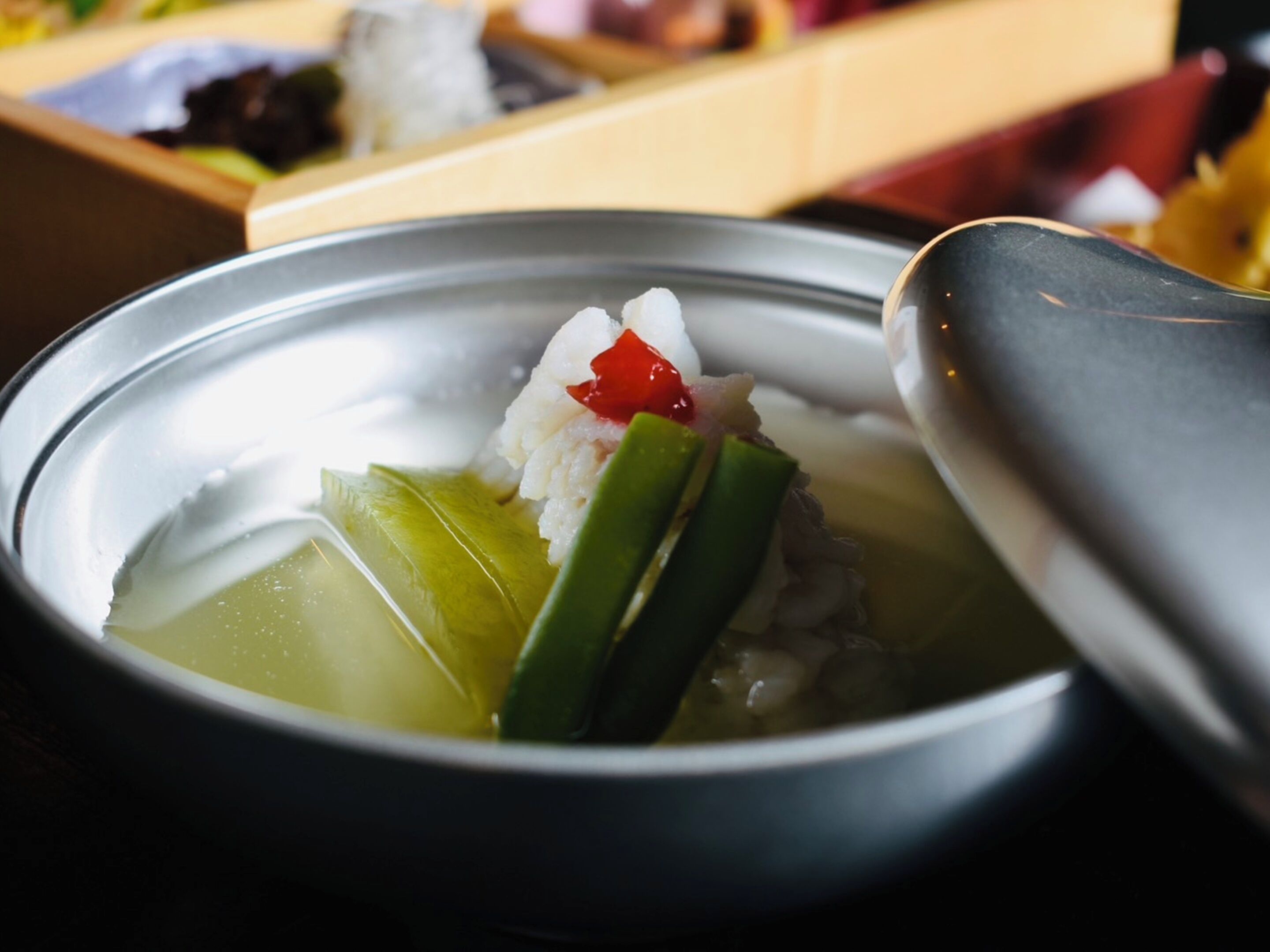 A bowl of soup with rice, green vegetables, and a red chili.